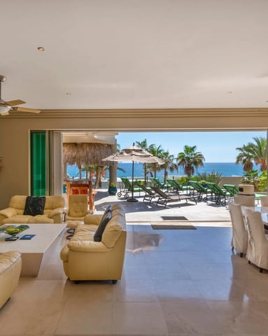 Sandy beach with turquoise water, rocky outcrops, and beachfront homes with palm trees under blue sky