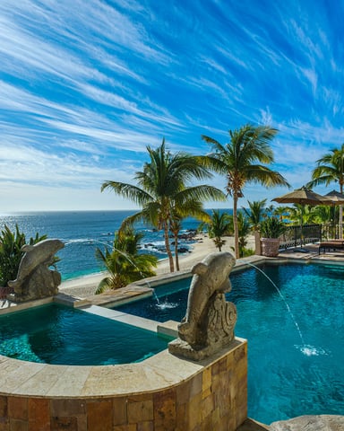 Infinity pool at sunset with palm trees reflected in still water and the ocean beyond