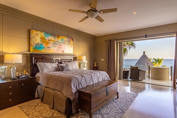 Beachfront villa patio with wooden lounge chairs, pool, palm trees, and ocean view