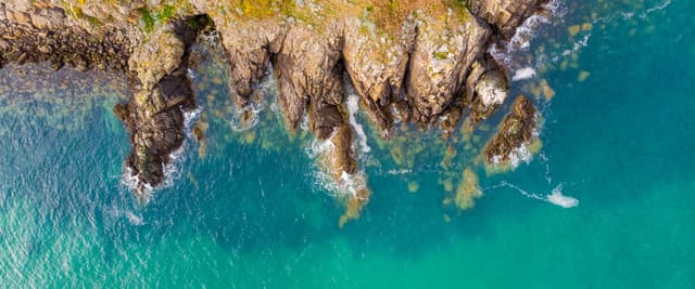 Aerial view of jagged coastal rock formations meeting turquoise water along a European shoreline