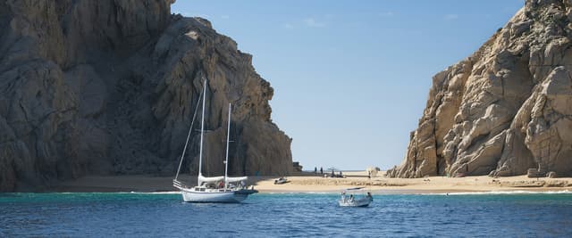 Sailboat anchored in calm turquoise water between dramatic rock formations at Cabo San Lucas