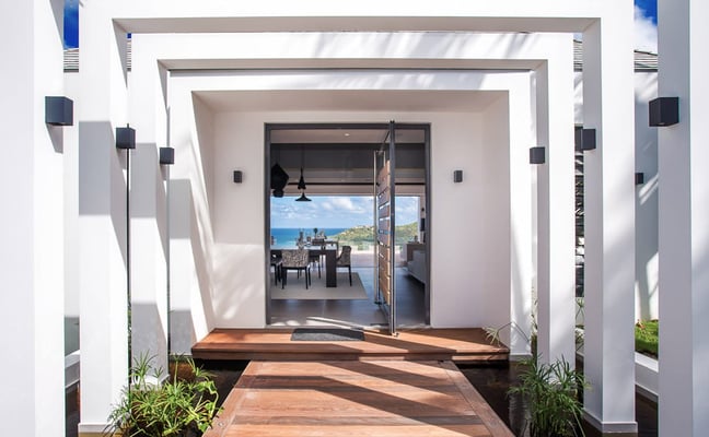 Open-plan living and dining room with ocean view, yellow leather seating, and direct access to beachfront terrace with lounge chairs and umbrellas